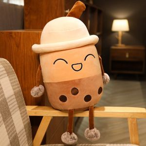 Plüschtier Bubble tea lacht mit einem Hut, ist beige und braun und sitzt auf der hölzernen Armlehne eines beige-weiß-braun karierten Sessels in einer Wohnung mit einer Lampe im Hintergrund