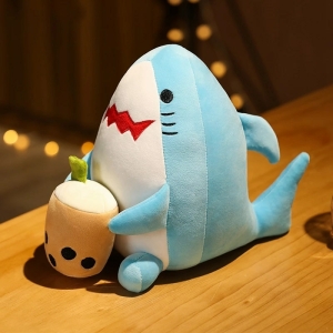Plüsch Bubble Tea in Form eines blauen Hais, der auf einem Holztisch sitzt und eine kleine beigefarbene Kanne in den Händen hält