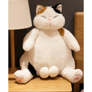 Eine große weiße Katze mit braunen und schwarzen Flecken sitzt auf einem Holztisch, eine weiße Nachttischlampe steht rechts von ihr