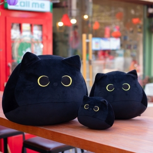 Drei schwarze Plüschkatzen in drei verschiedenen Größen. Auf einem Holztisch.