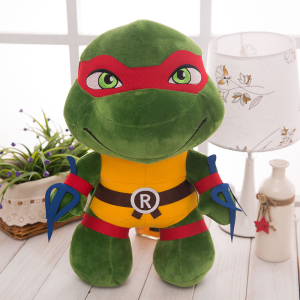 Plüsch-Ninja-Schildkröte mit rotem Stirnband und Zubehör, auf einem Tisch neben einer weißen Lampe und einer grünen Pflanze präsentiert